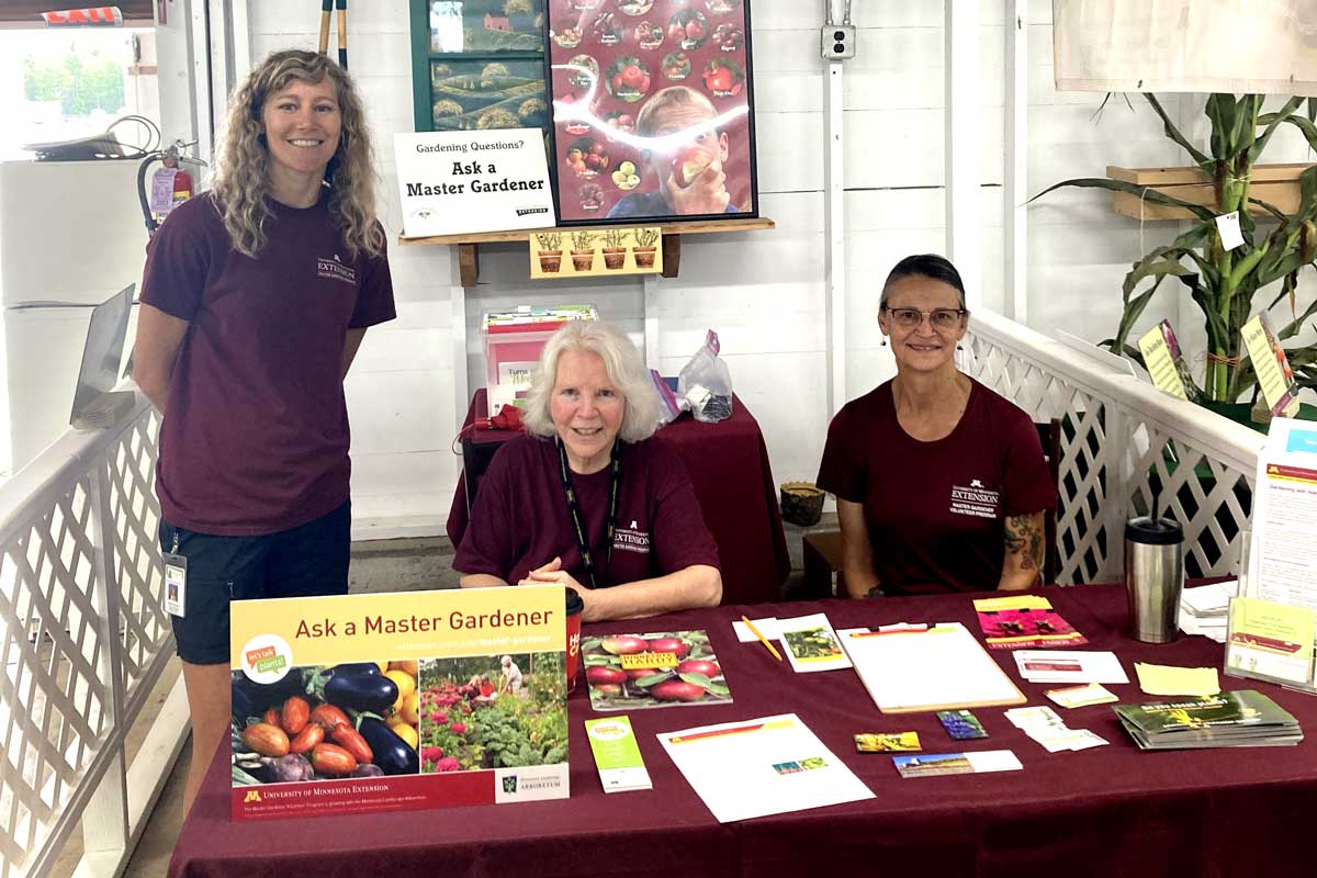 cwc-mg-crowwingcountyfair-1200px-hero Three women Master Gardener Volunteers sitting at an information booth at the Crow Wing County State Fair