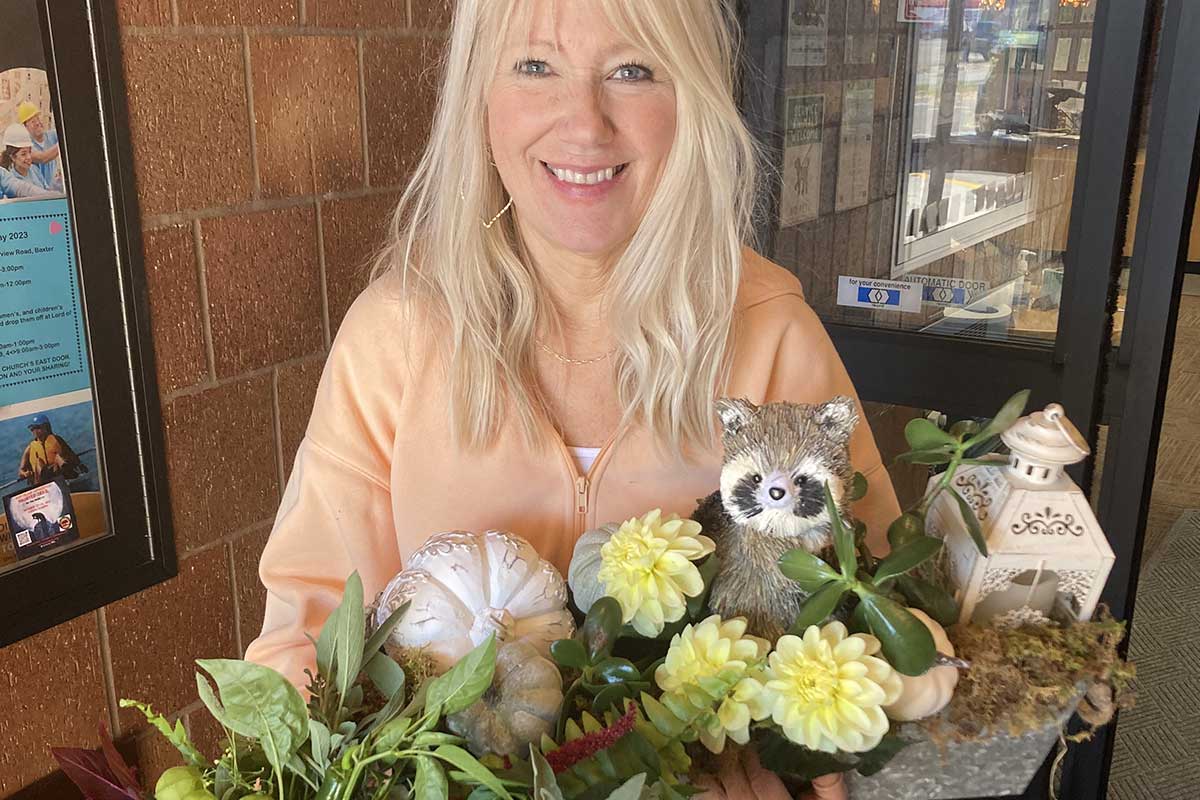 Smiling woman holds a decorative bouquet with flowers, a lantern, and a ceramic raccoon