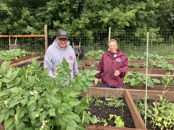 An older man and an older woman stand in a garden smiling at the camera
