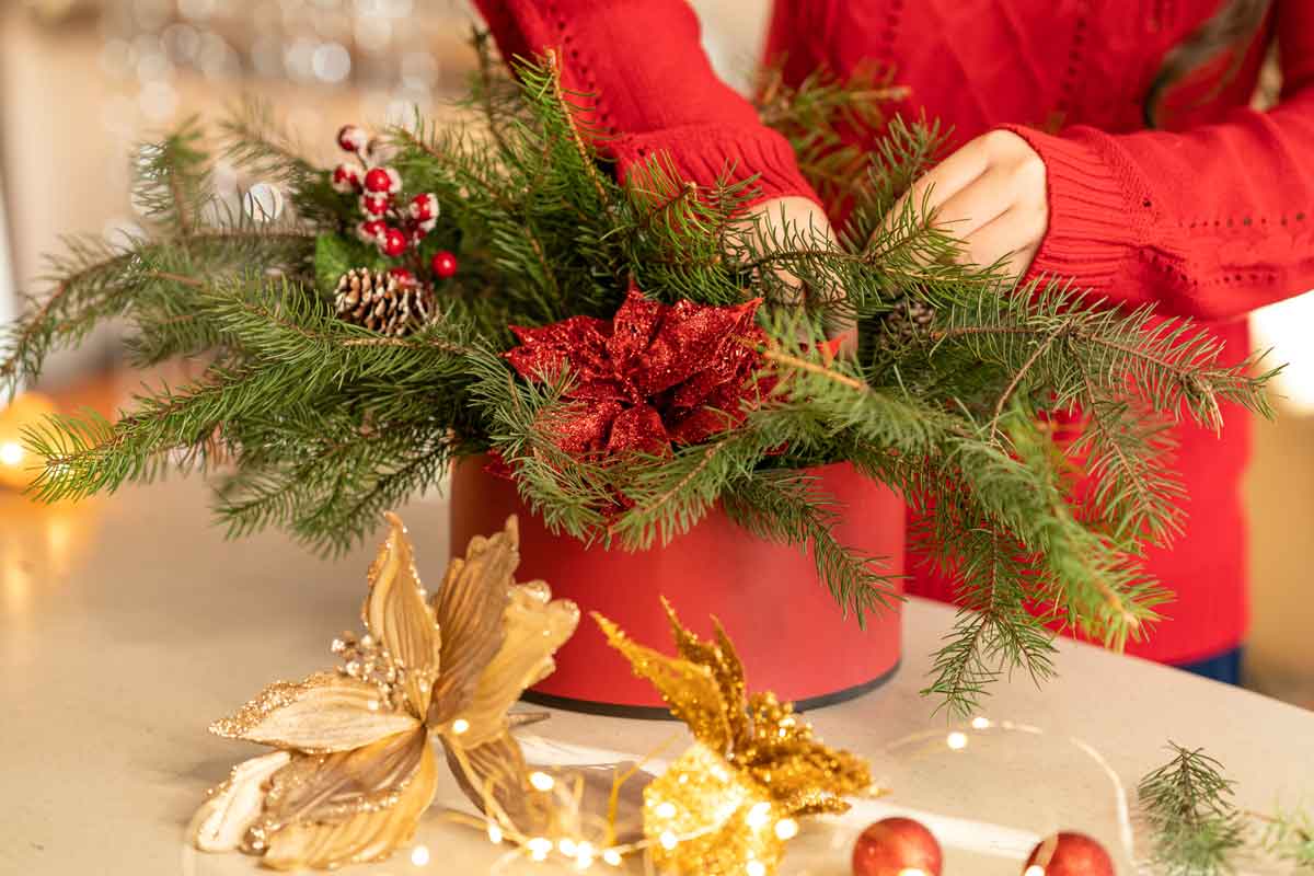 Person in a red sweater arranging greenery in a holiday pot